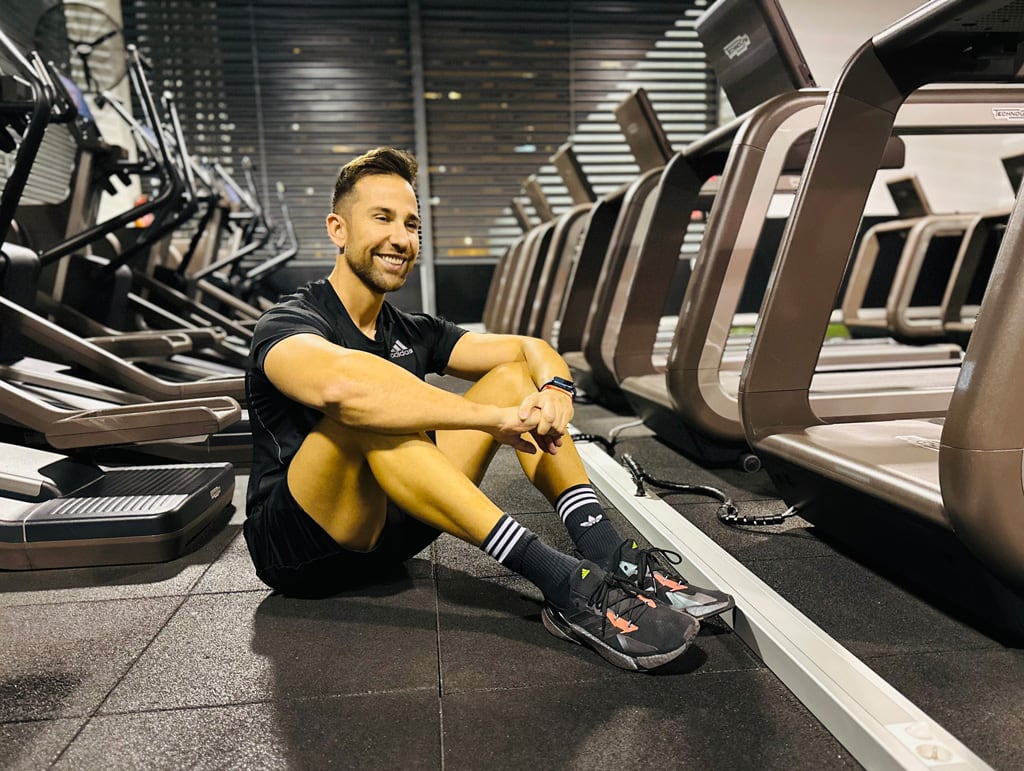 El entrenador está sentado en el suelo del gimnasio sonriendo.